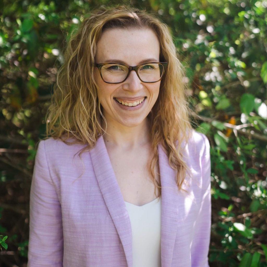 A picture of Michelle smiling. She is wearing glasses and a purple suit jacket.